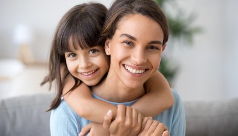 Young girl hugging her mother from behind