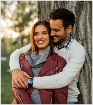 Smiling man and woman holding each other in front of tree