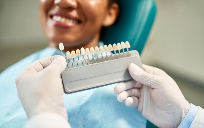 Cosmetic dentist helping smiling patient pick shade of veneer