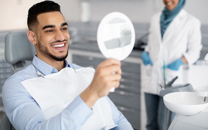 Man smiling at reflection in handheld mirror